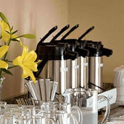 A table setup with coffee carafes, glassware, and yellow flowers.