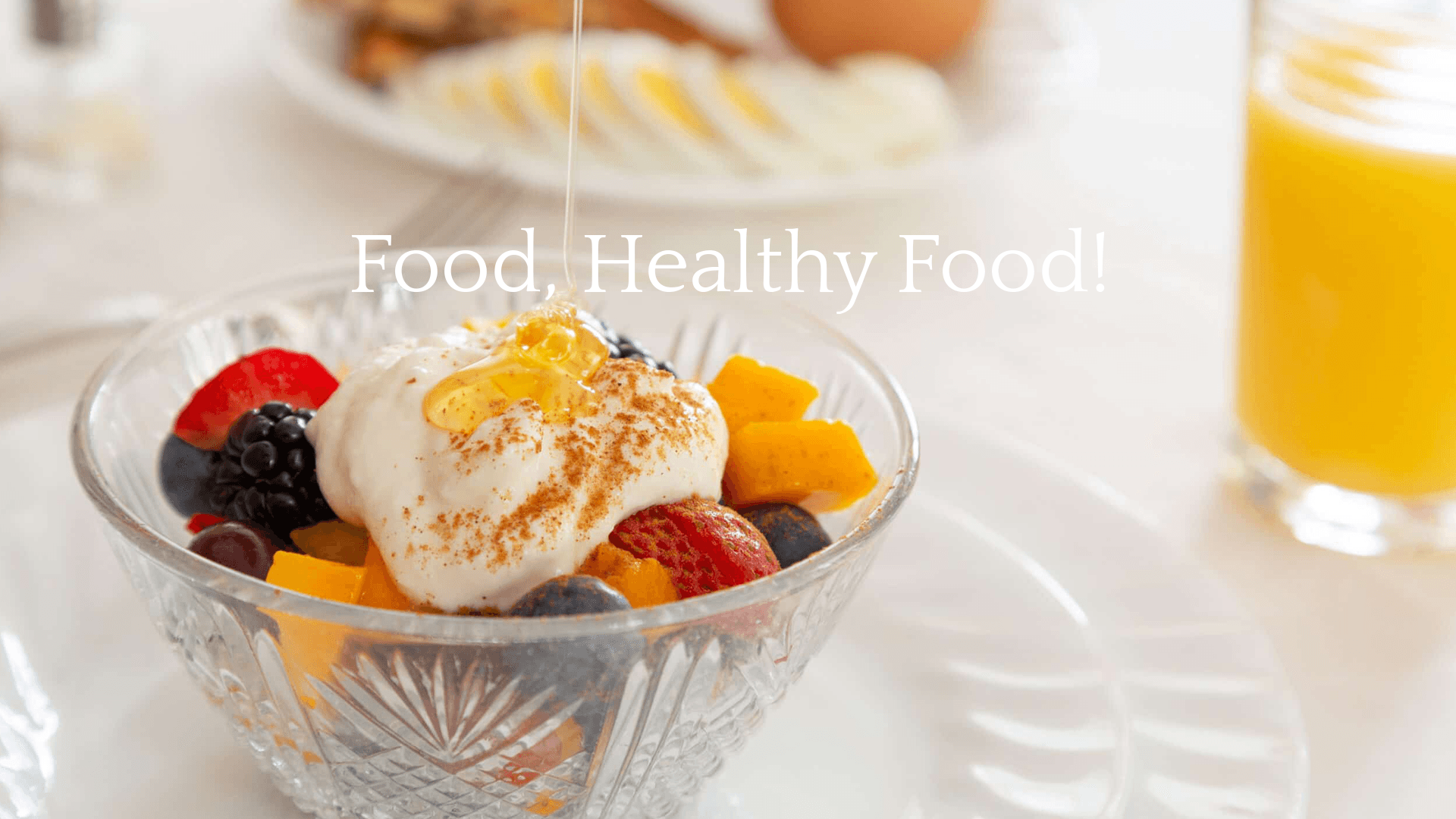 A bowl of yogurt topped with fresh fruit and honey, with a glass of orange juice in the background.