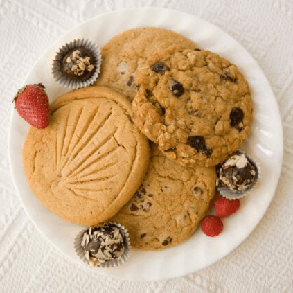 A plate of assorted cookies and chocolate truffles, accompanied by strawberries and raspberries.
