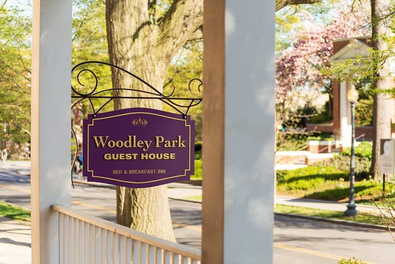 Sign for Woodley Park Guest House, a bed and breakfast inn, hanging in a tree-lined area.