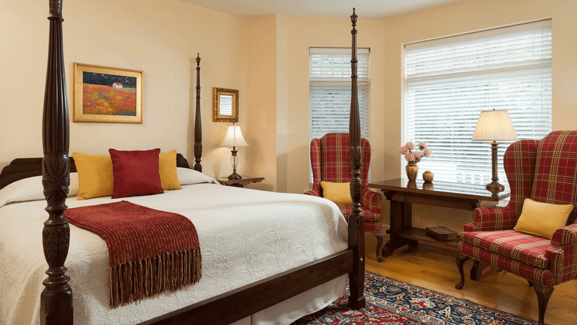 A cozy bedroom featuring a four-poster bed, colorful pillows, and two plaid armchairs.