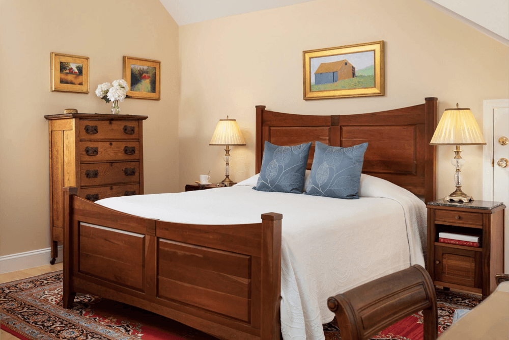 A cozy bedroom featuring a wooden bed, decorative pillows, a dresser, and soft lighting.