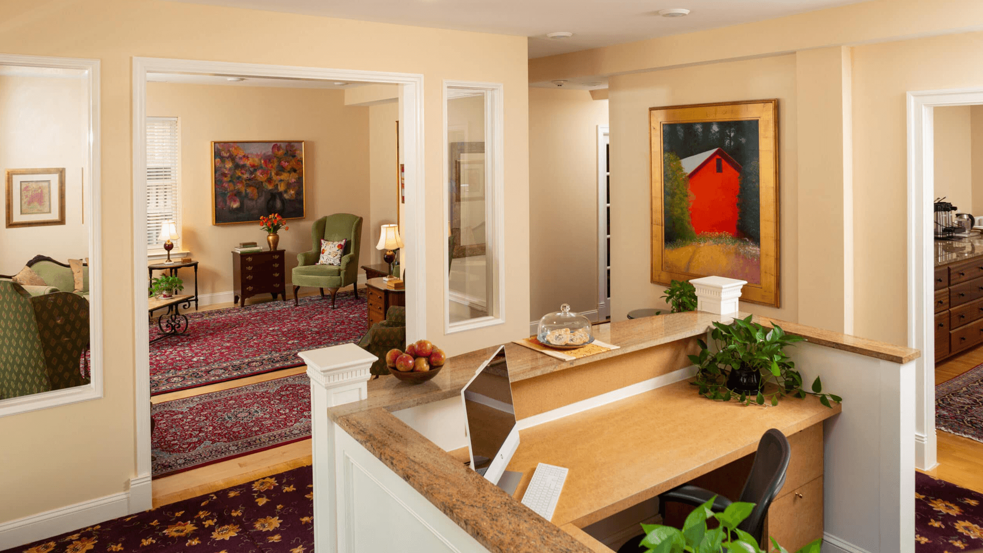 A bright and inviting reception area with a desk, plants, and cozy seating visible in adjacent rooms.